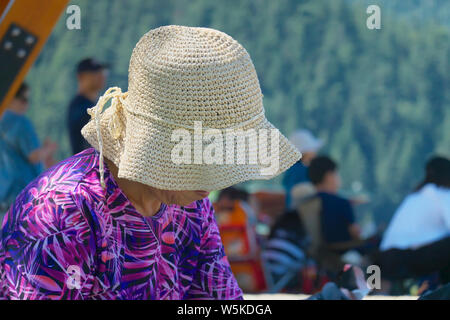 Una vista ravvicinata di un cappello di paglia su una donna che indossa un luminoso viola e rosa camicetta e guardando verso il basso. Foto Stock