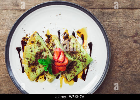 Indonesiano tradizionale frittelle di verde di guarnire con cioccolato e fragole fette. Il cibo della colazione concetto. Vista dall'alto. Foto Stock
