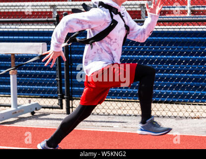 Alta scuola via e il campo runner è volata mentre strapped fino a e tirando una slitta di ponderata dietro di lui. Foto Stock