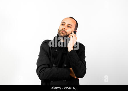 Uomo di mezza età con soprabito ascolta attentamente per una conversazione sul suo telefono cellulare, isolato su bianco. Foto Stock