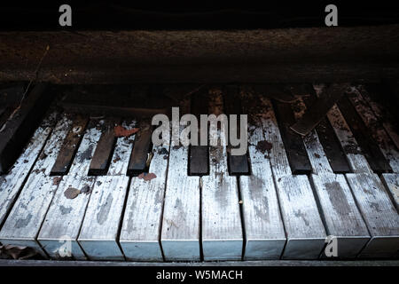 Primo piano delle chiavi sporche e danneggiate di un vecchio pianoforte verticale abbandonato lasciato a decadere Foto Stock