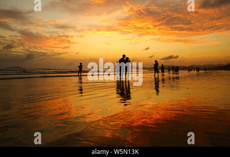 Persone godere il tempo libero tra la luminosità del tramonto sul mare nella città di Sanya, Cina del sud della provincia di Hainan, 22 aprile 2019. Foto Stock