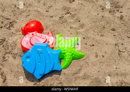 Giocattoli di sabbia sono fuori su una spiaggia di sabbia al sole: stampi di un rosso d'anatra, un pesce blu e una stella verde. Foto Stock