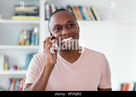 Americano africano con testa calva uomo maturo al telefono in ambienti chiusi in casa Foto Stock