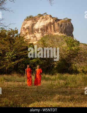 Negombo, Sri Lanka - 2019-03-22 - i monaci a piedi nel campo di erba con Roccia di Sigiriya in background. Foto Stock