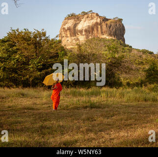 Negombo, Sri Lanka - 2019-03-22 - i monaci a piedi nel campo di erba con Roccia di Sigiriya in background. Foto Stock