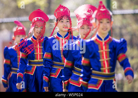 Il cinese studenti primari in costumi tradizionali e indossando il taglio della carta posa headwears presso una scuola in Huhhot, città del nord della Cina Foto Stock