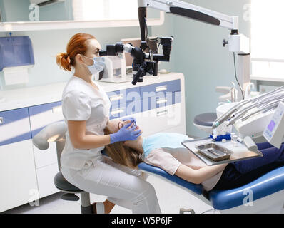 Dentista femmina con strumenti dentali - microscopio, specchio e sonda di trattare il paziente. Medicina e odontoiatria e cure sanitarie concetto. Foto Stock