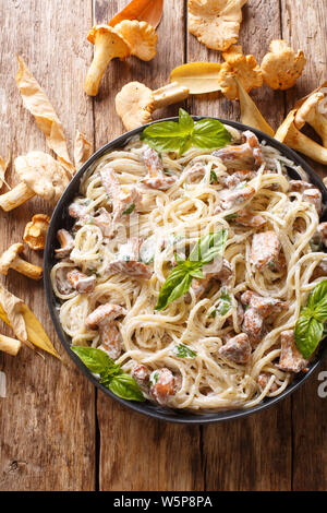 Spaghetti con finferli in salsa alla panna con basilico close-up su una piastra sul tavolo. Verticale in alto vista da sopra Foto Stock