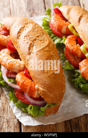 Sandwich con gamberetti, pomodori, peperoni, cipolle e lattuga fresca close-up su pergamena sulla tavola verticale. Foto Stock