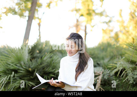 Femmina cinese studente seduto sul moncone nel parco e la lettura di carte. Concetto di preparazione prima di esame e donna asiatica. Foto Stock