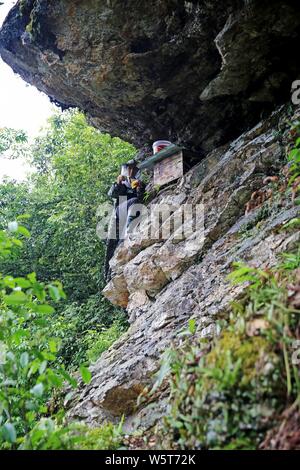 Un apicoltore si arrampica su una ripida scogliera di una montagna di raccogliere miele da alveari in legno in Rongshui Miao contea autonoma, Liuzhou city, a sud della Cina di Guan Foto Stock