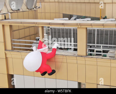 Un palloncino di giocattoli di Babbo Natale che porta un gigante borsa regalo è scalare la parete di un department store nella città di Nantong, est cinese della provincia di Jiangsu, 1 Decem Foto Stock