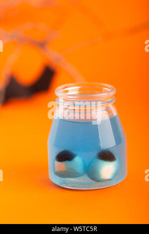 Concetto di Halloween - due occhi artificiali in un liquido di colore blu su sfondo arancione con bat e filiali su uno sfondo Foto Stock