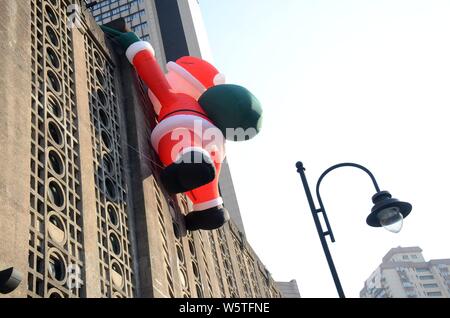 Un palloncino di giocattoli di Babbo Natale che porta un gigante borsa regalo è scalare la parete del 1933 Old Millfun in Cina a Shanghai, 18 dicembre 2018. Foto Stock