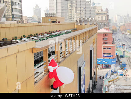 Un palloncino di giocattoli di Babbo Natale che porta un gigante borsa regalo è scalare la parete di un department store nella città di Nantong, est cinese della provincia di Jiangsu, 1 Decem Foto Stock