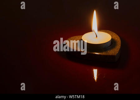 La luce di una candela su sfondo scuro Foto Stock