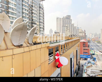 Un palloncino di giocattoli di Babbo Natale che porta un gigante borsa regalo è scalare la parete di un department store nella città di Nantong, est cinese della provincia di Jiangsu, 1 Decem Foto Stock