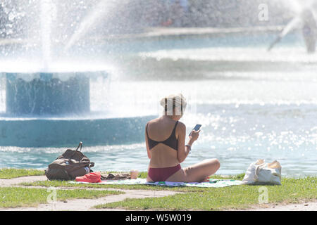 25/07/2019. Battersea, Londra, Regno Unito. Una donna si rilassa le fontane, nella calura del mezzogiorno in Battersea Park come un ondata di caldo spazza il Regno Unito. Foto Stock