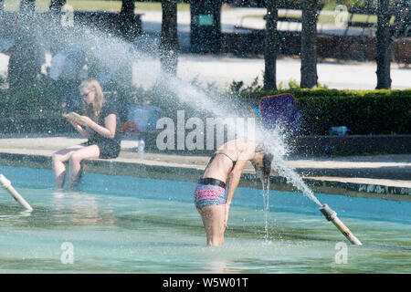 25/07/2019. Battersea, Londra, Regno Unito. Una donna non si raffredda in acqua fontane in Battersea Park come un ondata di caldo spazza il Regno Unito. Foto Stock