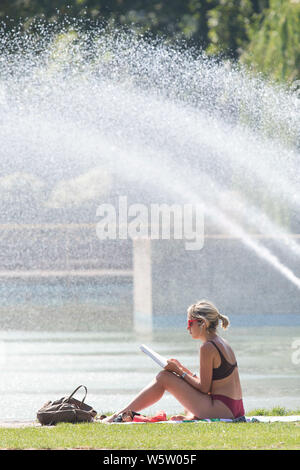 25/07/2019. Battersea, Londra, Regno Unito. Una donna che legge le fontane, nella calura del mezzogiorno in Battersea Park come un ondata di caldo spazza il Regno Unito. Foto Stock