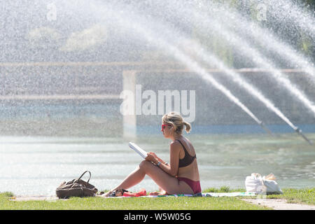 25/07/2019. Battersea, Londra, Regno Unito. Una donna che legge le fontane, nella calura del mezzogiorno in Battersea Park come un ondata di caldo spazza il Regno Unito. Foto Stock