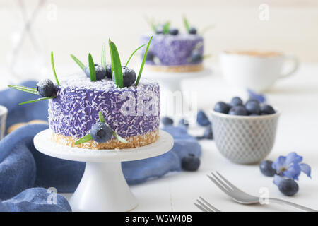 Due round non cuocere fragola mini cheesecake con sale di caramello e halfs di fragole, abbellito con veri fiori blu. Blue tavolo in legno. Foto Stock