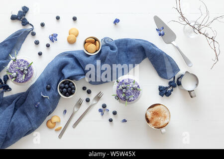 Due round non cuocere fragola mini cheesecake con sale di caramello e halfs di fragole, abbellito con veri fiori blu. Blue tavolo in legno. Foto Stock