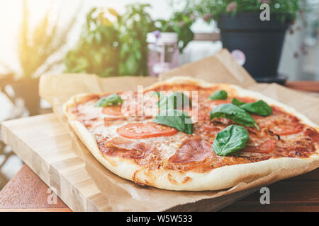 Freschi Fatti in casa con la pizza serrano, pomodori a fette e di foglie di basilico fresco sul tavolo di legno sul patio Foto Stock