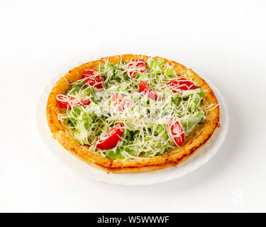 Caesar pizza con pollo su una piastra laterale. Formaggio a pasta dura in forma di foglie di insalata. Pomodori a fette. Su uno sfondo bianco, close-up. Vista laterale Foto Stock