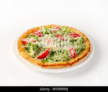 Caesar pizza con pollo su una piastra laterale. Mozzarella grattugiato. Foglie di insalata. Pomodori a fette. Su uno sfondo bianco, close-up. Vista laterale Foto Stock