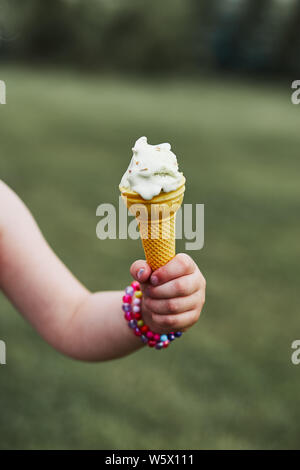 Stretta di mano childs tenendo cono con gelato su una pianura verde naturale dello sfondo. Candide persone, veri momenti e situazioni reali Foto Stock