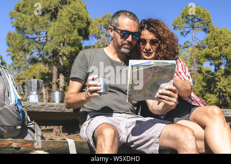 Paio di prendere un periodo di riposo dopo il trekking l uomo e la donna che guarda la mappa per trovare il percorso di trekking Caucasian persone bere un caffè in una giornata di sole a Foto Stock