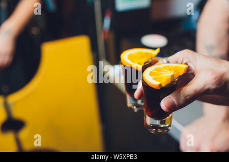 Mani maschio allegria con bicchieri di shot o liquore. Amici bere shot o liquore e cheers. Maschio di allietare le mani con alcool sulla barra sfocata sullo sfondo Foto Stock