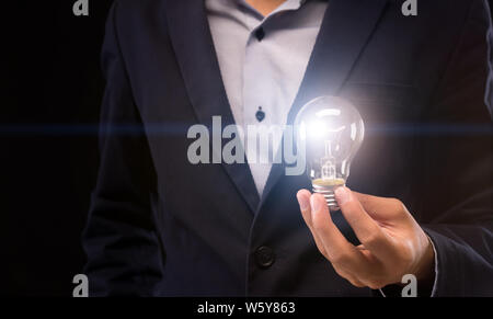 Imprenditore con lampadina in mano su sfondo nero Foto Stock