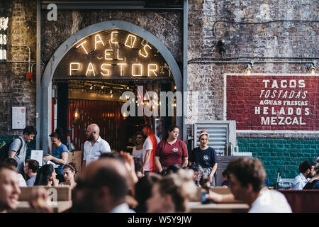 London, Regno Unito - Luglio 23, 2019: persone sedute a tavoli all aperto di El Pastore Tacos ristorante nel mercato di Borough, uno dei più grandi e più antiche cibo m Foto Stock