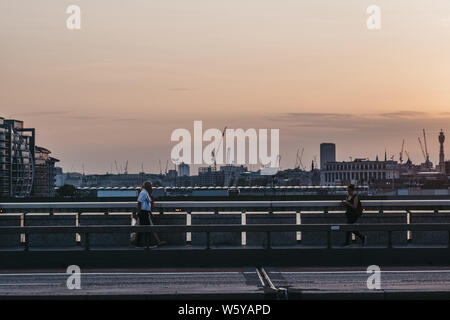 London, Regno Unito - Luglio 23, 2019: persone camminando sul Ponte di Londra al tramonto, il fuoco selettivo, città sullo sfondo. Londra è una delle città più visitate Foto Stock