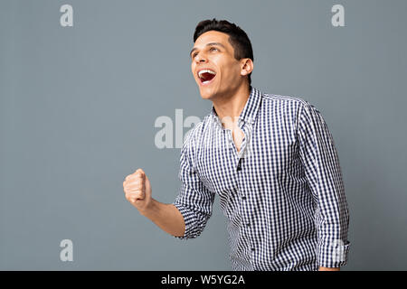 Felice ragazzo arabo scuotendo pugno chiuso su sfondo grigio Foto Stock