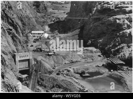 Vista guardando a monte attraverso canyon nero mostra a valle paratoia e rock risacca barriera. Scavo nella sottostruttura dam ed a monte di paratoia visto in background. Costruzione di uffici e negozi visto sulle creste delle paratoie. Stoney struttura di gate al portale di uscita del tunnel di deviazione n. 2 visto in basso a sinistra.; Portata e contenuto: fotografia dal volume due di una serie di album di foto per documentare la costruzione della Diga di Hoover, Boulder City, Nevada. Foto Stock