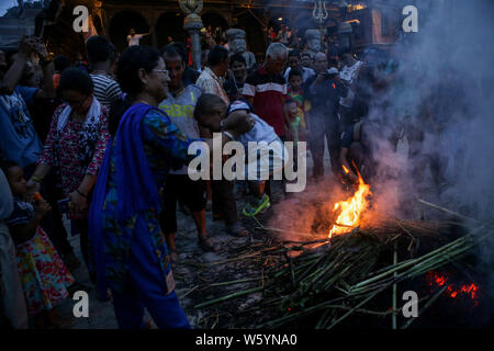 Una donna oscilla un bambino attorno a un fuoco ardente da un'effigie del demone Ghantakarna a simboleggiare la distruzione del male durante il Gathamuga o festival Ghantakarna.Nepalese credono che il festival nei reparti gli spiriti maligni, e porta la pace e la prosperità. Foto Stock