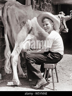 1940s sorridente ragazzo biondo seduto su uno sgabello indossando cappello di paglia di mungere una mucca - d1173 HAR001 HARS a metà lunghezza di allevamento bovino maschi fiducia AGRICOLTURA B&W OBIETTIVI FELICITÀ ALLEGRO CHORE GLI AGRICOLTORI DI MUNGITURA ORGOGLIO SORRISI DAIRYING COLLEGAMENTO gioiosa cooperazione novellame pre-teen pre-teen BOY compito in bianco e nero di etnia caucasica HAR001 in vecchio stile Foto Stock