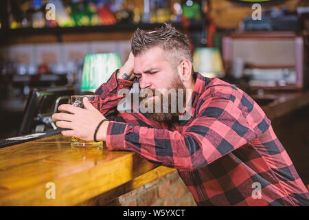 Il bar è un luogo rilassante hanno bere e rilassarsi. Uomo con barba trascorrere il tempo libero nella barra di colore scuro. Brutale parigamba uomo barbuto sedersi al banco bar bere birra. Hipster rilassante presso il bar con birra. Ordine di bere alcol. Foto Stock