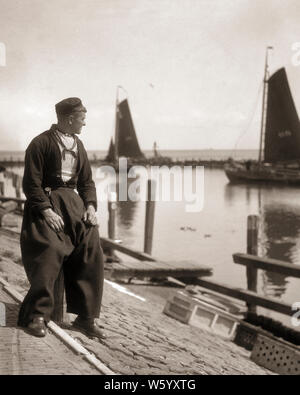 1920s uomo pescatore in abiti tradizionali BARCHE A VELA IN BACKGROUND del porto di Volendam OLANDA - r3740 HAR001 HARS TRASPORTO B&W HARBOR abilità Competenze occupazione pantaloni velieri turistico in occupazioni di attrazione HOLLAND popolare concettuale elegante barca da pesca MID-adulto metà uomo adulto BIANCO E NERO ETNIA CAUCASICA HAR001 Paesi Bassi in vecchio stile Foto Stock