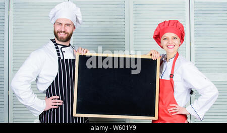 Imparando a cucinare attraverso il cuoco. Maestro Cuoco e cucina cameriera dando lezioni di cucina. Coppia di un uomo e di una donna che mantiene la scheda vuota nella scuola di cucina. Chef e insegnamento helper master class, copia dello spazio. Foto Stock