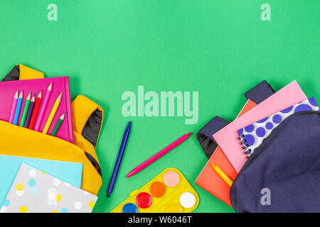 Si torna a scuola concetto. Giallo e blu zaini con forniture scolastiche, libri e quaderni su sfondo verde chiaro. Vista superiore Foto Stock