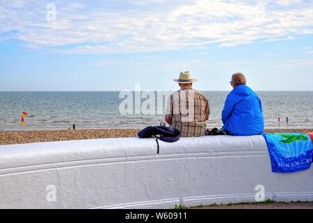 Vista posteriore di una coppia di anziani seduti su un muro sul lungomare che si affaccia sul mare da una giornata d'estate, Bognor West Sussex England Regno Unito Foto Stock