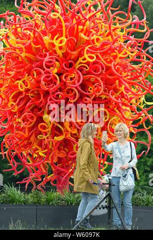 Due donne che assumono selfies contro una spettacolare sculture in vetro di Dale Chihuly sul display a Kew Giardini Botanici di West London Inghilterra England Regno Unito Foto Stock