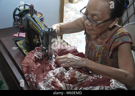 Dortje Nony, 73, cuce un panno in casa sua. Mrs.Nony si prende cura del suo marito Andarias Sarra, 80, una corsa vittima che sopravvivere da due attacchi di corsa Foto Stock