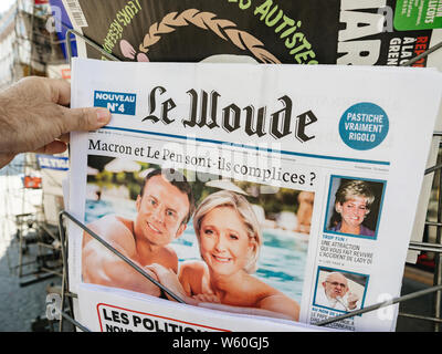 Parigi, Francia - Lug 24, 2019: Man mano che tiene il satirico Le Woude quotidiano a French press kiosk con collage del presidente francese Emmanuel Macron e Marine Le Pen Foto Stock