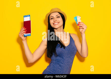 Giovani sorridente Excited donna studente azienda passaporto carta di imbarco del biglietto e della carta di credito isolato su sfondo giallo. Volo - Immagine Foto Stock